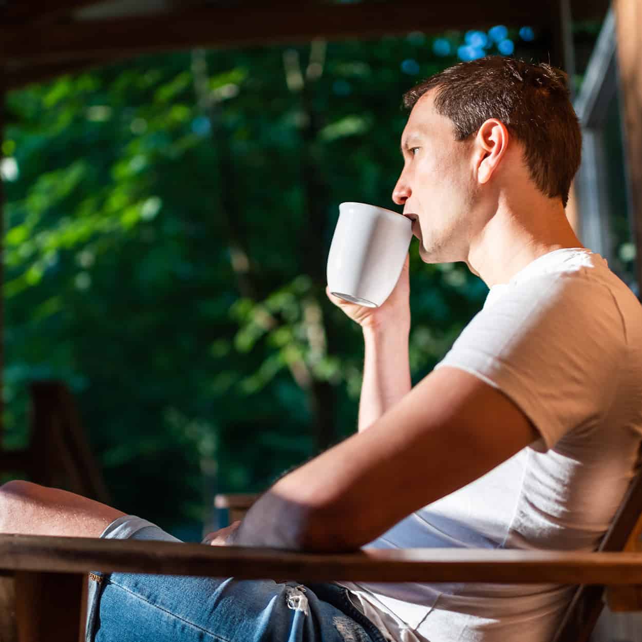 man sitting and drinking coffee on cabin deck during at-home addiction rehab