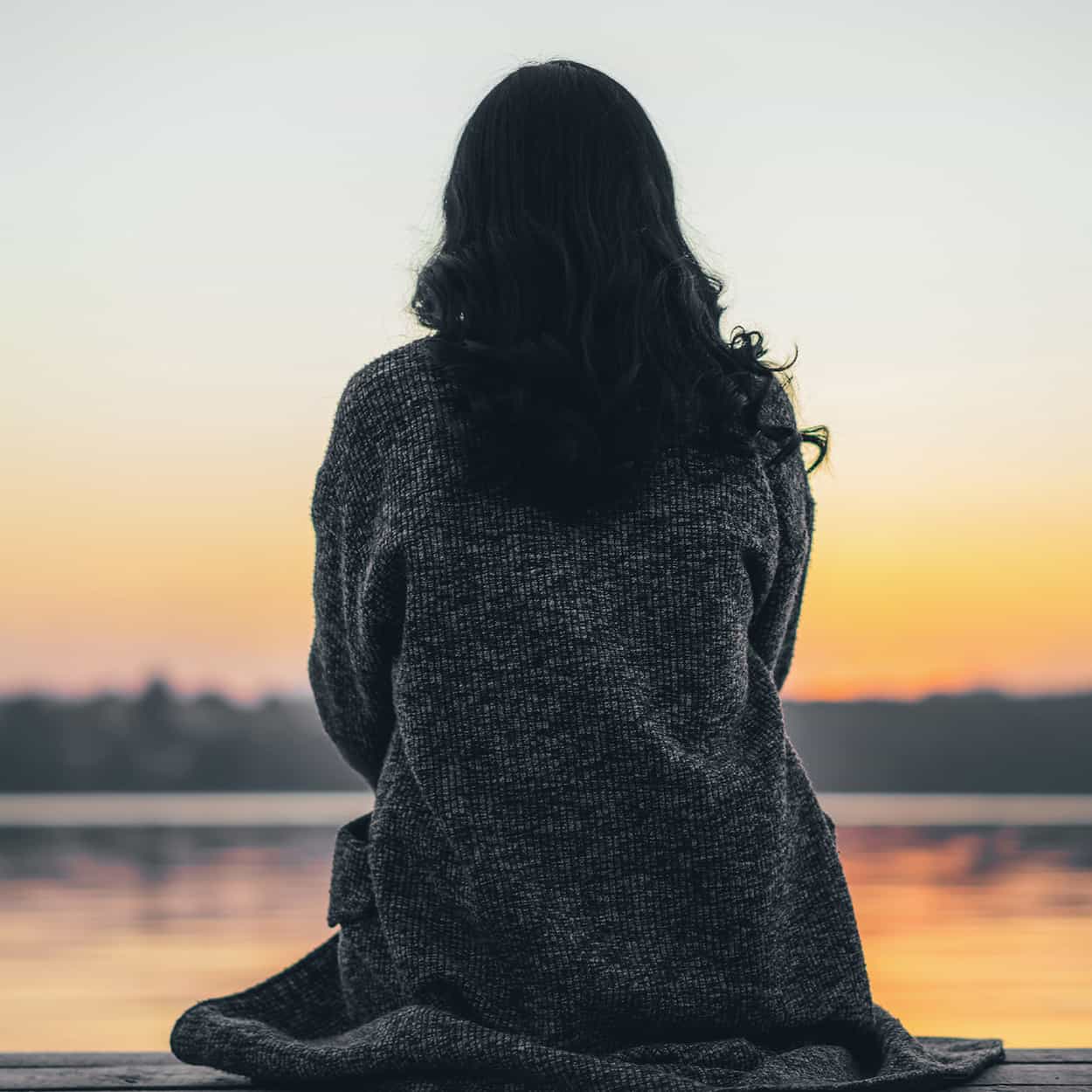 woman sitting and thinking by a lakeside sunset during at-home addiction rehab