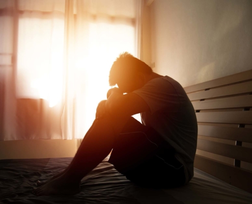 desperate man in silhouette sitting on the bed with hands on head