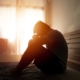 desperate man in silhouette sitting on the bed with hands on head