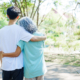 A happy senior mother embraces her smiling adult son in a lush green park