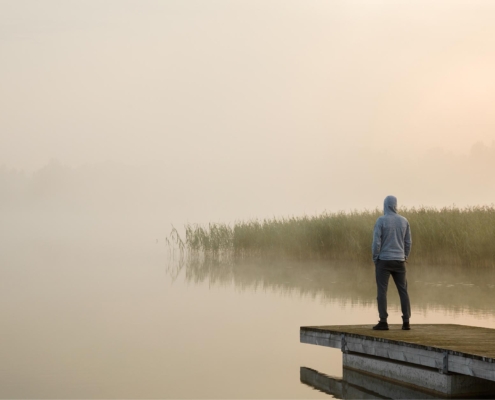 Person standing on edge of footbridge and staring at lake.