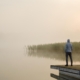 Person standing on edge of footbridge and staring at lake.