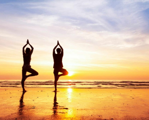 Two people doing yoga next to the beach at sunset
