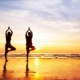 Two people doing yoga next to the beach at sunset
