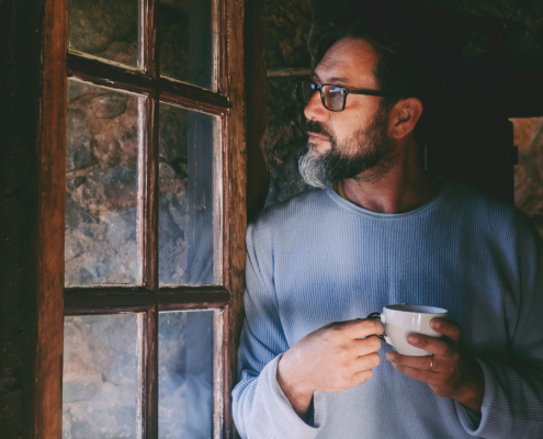 Serene and relaxed mature man standing indoor at home near the window