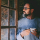 Serene and relaxed mature man standing indoor at home near the window