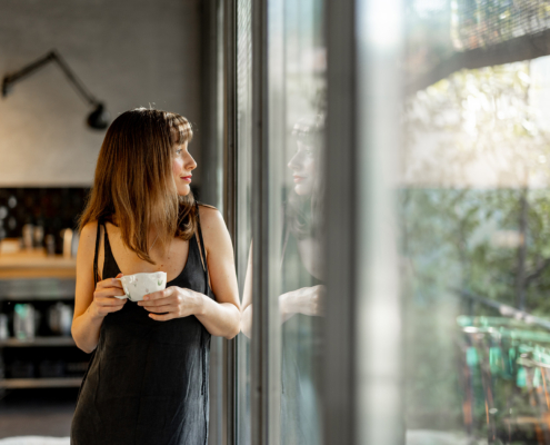 A relaxed woman in a minimalist dress leans on a rustic dining table